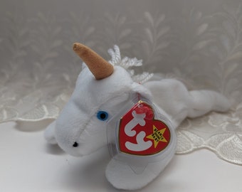 Könnte beinhalten: Weißes Einhorn Beanie Baby mit goldenem Horn und blauem Auge. Das Etikett lautet "Beanie Baby" mit einem roten Stern.
