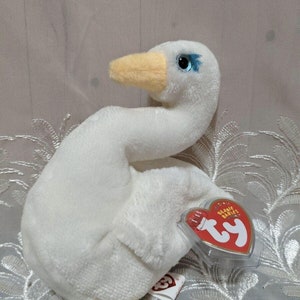 Peut inclure: Peluche de cygne blanc en forme de beanie baby avec un bec jaune et des yeux bleus. Le beanie baby a une étiquette Ty attachée.