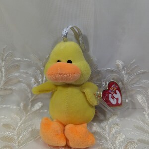 May include: Yellow plush duck with orange feet and beak. The duck has a small, clear plastic tag with the text "Beanie Babies" and the number "3" on it.