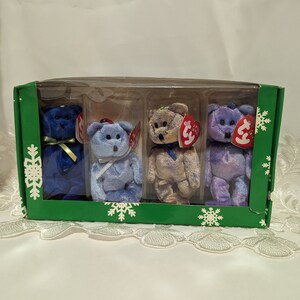 Può includere: Un set di quattro Beanie Babies blu, viola e dorati in una scatola verde con disegni di fiocchi di neve. I Beanie Babies indossano tutti i loro caratteristici cartellini rossi.