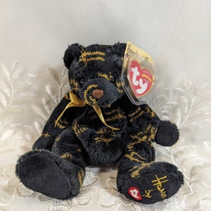 May include: Black and gold striped Ty Beanie Baby with a yellow ribbon around its neck. The tag reads "Ty Beanie Babies" and "Harrods".