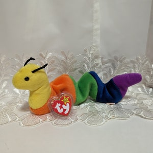 May include: A yellow and rainbow striped beanie baby worm with a Ty tag. The worm has black eyes and a black nose.