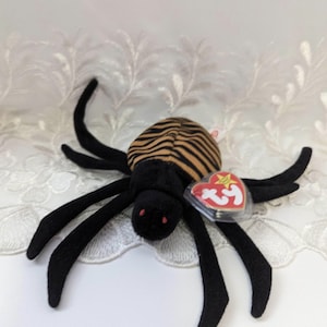 May include: Black and orange striped spider plush toy with red eyes. The toy has a Ty tag attached to one of its legs.