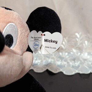 May include: A plush Mickey Mouse toy from the Beanie Buddies Collection. The tag is a heart shape with the text "Mickey" and "www.ty.com". The tag also has a Disney logo.