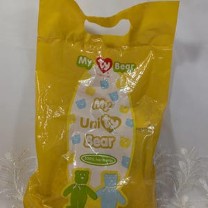 May include: Yellow plastic bag featuring a Ty Bear logo and the text "My Unity Bear 100% Harmony". The bag contains two plush bears, one green and one blue.