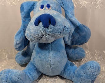 Könnte beinhalten: Ein blaues Plüsch-Hundespielzeug mit großen, weißen Augen und einer blauen Nase. Der Hund sitzt mit ausgestreckten Beinen.