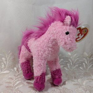 May include: A soft pink unicorn toy with a magenta mane and tail. The toy has a textured body with darker pink accents on its legs. A small tag is attached to the ear.
