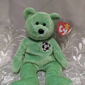 May include: Green Beanie Baby plush toy with a football on its chest. The bear has black eyes and a black nose. The tag reads "Beanie Baby" and "ty".