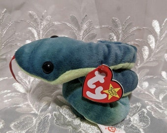 Pode incluir: Um brinquedo de pelúcia em forma de cobra em tons de verde-azulado e verde, com olhos grandes e pretos e uma língua vermelha. O brinquedo tem uma etiqueta vermelha em forma de coração que diz "Beanie Babies" e uma etiqueta menor que diz "Hissy".