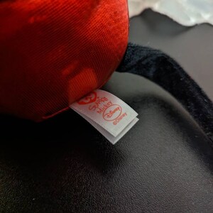 May include: A close-up of a red and black plush toy with a white tag that reads "Special Mickey Disney".