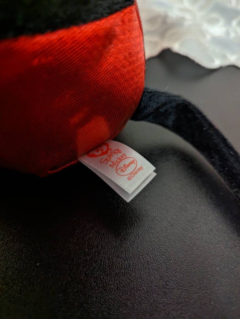 May include: A close-up of a red and black plush toy with a white tag that reads "Special Mickey Disney".