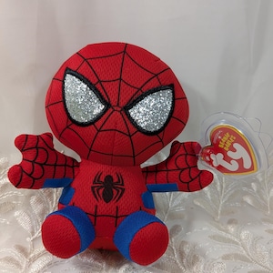 May include: A red Spider-Man soft toy with a black spider emblem on the chest and blue detailing. The toy features glittery silver eyes and a red web pattern. A clear tag with "Original Beanie Babies" is attached.