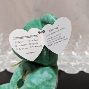 Peut inclure: Peluche verte Beanie Baby nomm&eacute;e Killarney avec un patch arc-en-ciel. L'&eacute;tiquette indique "Date de naissance : 17 mars 2003" et comprend un po&egrave;me sur un pot d'or au bout de l'arc-en-ciel. L'&eacute;tiquette indique &eacute;galement les informations de la soci&eacute;t&eacute; Ty Inc. et son site web.
