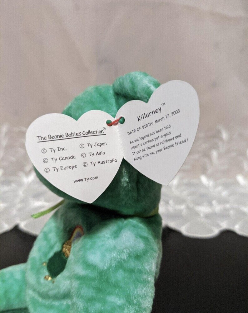 Peut inclure: Peluche verte Beanie Baby nomm&eacute;e Killarney avec un patch arc-en-ciel. L'&eacute;tiquette indique "Date de naissance : 17 mars 2003" et comprend un po&egrave;me sur un pot d'or au bout de l'arc-en-ciel. L'&eacute;tiquette indique &eacute;galement les informations de la soci&eacute;t&eacute; Ty Inc. et son site web.