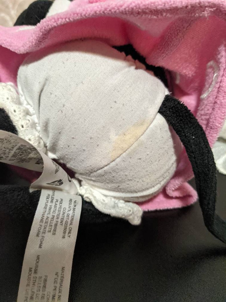 May include: A pink and black plush toy with a white fabric lining. The toy has a tag attached that reads "NEW MATERIAL ONLY REG.NO 057-02250916 CONTENT POLYESTER FIBRES PLASTIC PELLETS HYLENE VINYL ACETATE FOAM POLYURETHANE FOAM MAT&Eacute;RIAUX NE NDE PERMI CON FIBRES DE MOUSSE STHI L&Ecirc;NE BILLES DE MOUSSE DE PG".