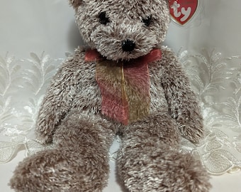 May include: A plush brown teddy bear with a red and gold ribbon around its neck. The bear has a Ty heart-shaped tag attached. The bear is sitting with its legs extended.