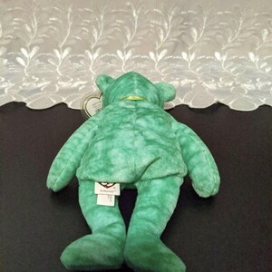 Peut inclure: Ours en peluche Beanie Baby vert tie-dye avec un ruban vert autour du cou. L'ours est couch&eacute; sur le dos, les pattes en l'air. L'ours a une &eacute;tiquette Ty attach&eacute;e &agrave; son pied qui dit "Beanie Babies" et "Ty Inc."