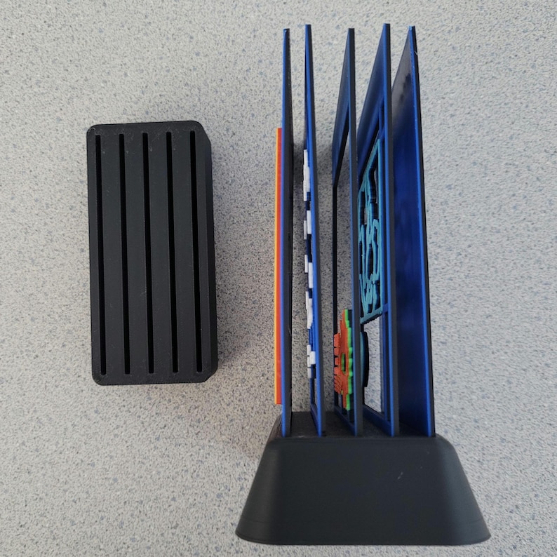 May include: A black plastic stand with a blue and orange multi-layered design. The stand has a rectangular base and a series of vertical slots. The stand is designed to hold and display multiple items.