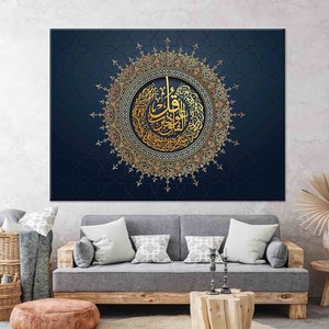 Puede incluir: Una gran obra de arte en lienzo con caligraf&iacute;a &aacute;rabe dorada dentro de un dise&ntilde;o circular ornamentado. La obra de arte est&aacute; sobre un fondo azul oscuro con un sutil patr&oacute;n geom&eacute;trico. La pieza se exhibe sobre un sof&aacute; gris.