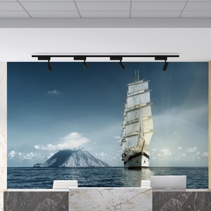 May include: A white sailboat with sails billowing in the wind, sailing on a calm blue ocean with a small island in the background. The scene is depicted on a large wall mural behind a marble reception desk.