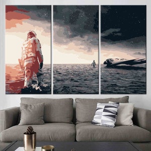 Pode incluir: Uma impressão em tela de três painéis que retrata um astronauta caminhando na água, com uma nave espacial ao longe. A obra de arte apresenta uma paleta de cores de vermelhos, cinzas e azuis suaves, evocando uma sensação de isolamento e aventura. O céu está cheio de estrelas.