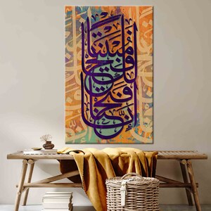 K&ouml;nnte beinhalten: Leinwanddruck mit aufwendiger violetter arabischer Kalligraphie vor einem farbenfrohen Hintergrund aus Orange, Blau und Gr&uuml;n. Das Kunstwerk wird an einer Wand &uuml;ber einer Holzbank ausgestellt.