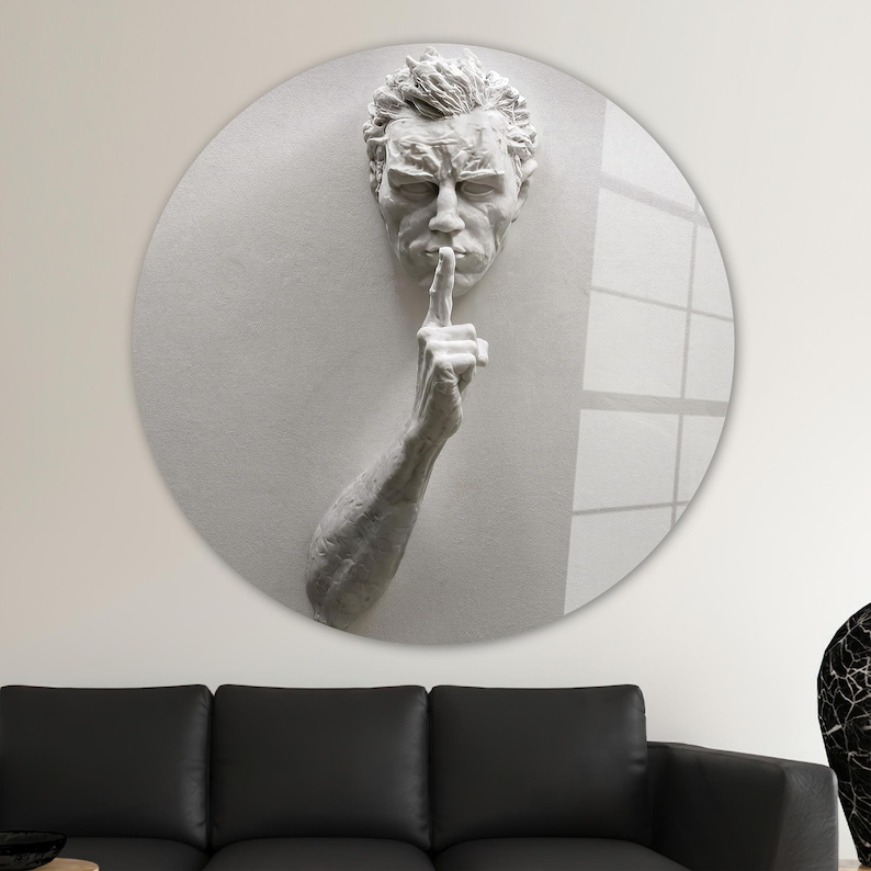 Pu&ograve; includere: Una scultura tridimensionale bianca di una testa e un braccio umani, con il dito sulle labbra, come per dire "shhh". La scultura &egrave; montata su uno sfondo bianco rotondo.