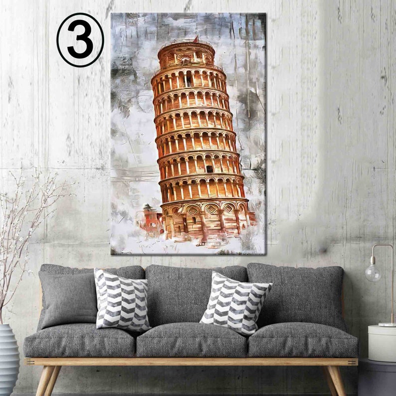 May include: A canvas print of the Leaning Tower of Pisa, rendered in warm tones of gold and brown against a textured, abstract background. The artwork is displayed above a gray sofa with decorative pillows.