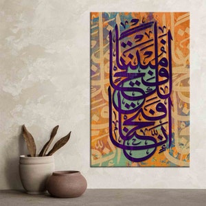 K&ouml;nnte beinhalten: Vertikales Leinwandbild mit arabischer Kalligraphie in Lila vor einem strukturierten Hintergrund in Orange, Blau und Gr&uuml;n. Das Kunstwerk h&auml;ngt an einer neutralen Wand. Eine kleine Vase und dekorative Elemente befinden sich im Vordergrund.