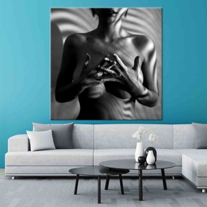 May include: Black and white canvas art print featuring a person with hands clasped in front of their chest. The background has a striped pattern. The artwork is displayed above a gray sofa and black coffee tables.