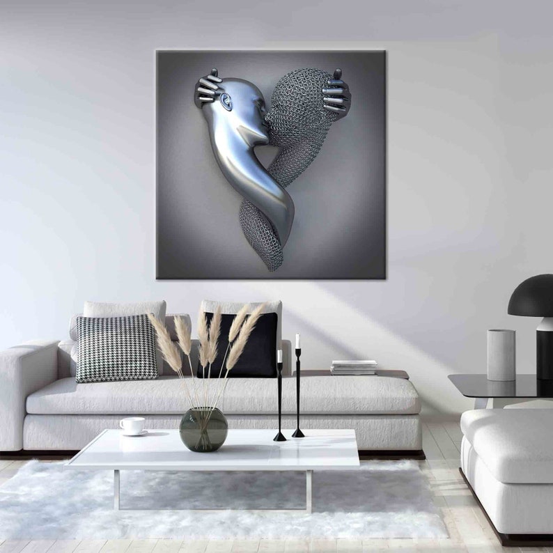 Op de afbeelding: Een grote, metalen sculptuur van twee figuren die elkaar omarmen en een hart vormen. E&eacute;n figuur is glad en zilverkleurig, de andere is getextureerd. Het kunstwerk hangt aan een grijze muur boven een witte bank en salontafel.