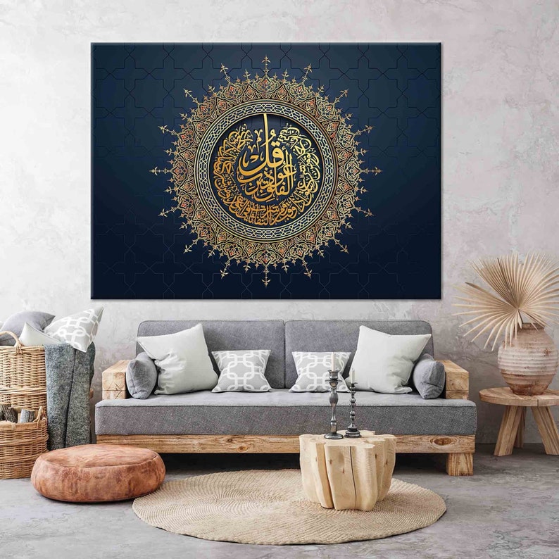 Puede incluir: Una gran obra de arte en lienzo con caligraf&iacute;a &aacute;rabe dorada dentro de un dise&ntilde;o circular ornamentado. La obra de arte est&aacute; sobre un fondo azul oscuro con un sutil patr&oacute;n geom&eacute;trico. La pieza se exhibe sobre un sof&aacute; gris.