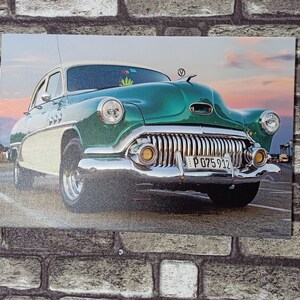 May include: A vintage green car with chrome accents and a white number plate that reads "P 075 912". The car is parked on a tarmac road with a brick wall in the background.