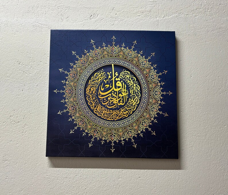 Puede incluir: Arte en lienzo cuadrado con caligraf&iacute;a &aacute;rabe dorada dentro de un dise&ntilde;o circular, sobre un fondo azul oscuro con un patr&oacute;n geom&eacute;trico. La obra de arte tiene un borde detallado y adornado.