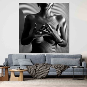 May include: Black and white art print of a person with hands clasped in front of the chest. The person's torso is visible, with light and shadow creating a striped pattern on the background. The artwork is displayed above a blue sofa.