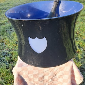 May include: A black ice bucket with a white logo of a shield shape. The bucket is sitting on a pink and white checkered cloth.