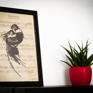 Op de afbeelding: Een ingelijst afdruk van bladmuziek met een zwart silhouet van twee mensen die elkaar omhelzen. De muziek is getiteld "Balammb Garden Final Fantasy VIII". De afdruk staat op een plank naast een groene plant in een rode pot.