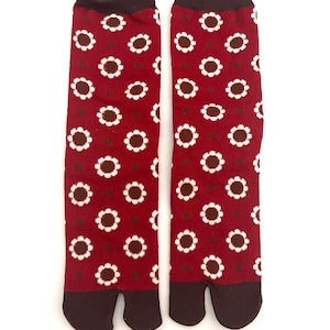 May include: A pair of red tabi socks with a white and brown floral pattern. The socks have a split toe design and a dark brown cuff and toe section. The socks are displayed on a white background.