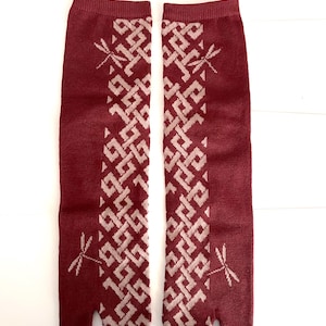 May include: A pair of deep red tabi socks featuring a light pink geometric lattice pattern running vertically down the center. Each sock is adorned with two small dragonfly motifs, one near the top and one near the bottom, and has a split-toe design.