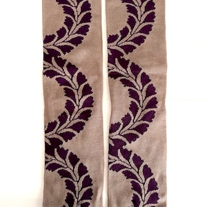May include: A pair of split-toe socks featuring a light brown base color with a repeating dark purple leaf vine pattern. The socks have a solid dark purple cuff at the top and a distinct separation between the big toe and the other toes.