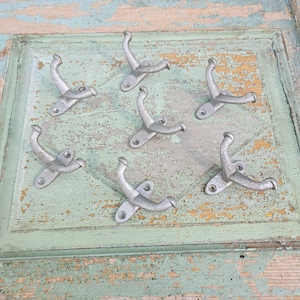 May include: A collection of six silver-toned metal wall hooks arranged in a circular pattern. Each hook features a central mounting plate with two screw holes and a double-pronged design with one hook curving upward and one curving outward.