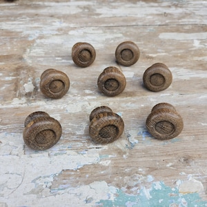 Può includere: Un set di otto pomelli rotondi in legno con una finitura marrone naturale e un centro circolare incassato. Ogni pomello presenta una venatura del legno visibile e un bordo liscio e arrotondato, progettato per il fissaggio su mobili.
