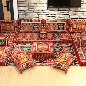 May include: A large, ornate floor seating set with a traditional Middle Eastern design. The set features red, green, and gold patterned cushions and rugs. The arrangement includes multiple seating sections, pillows, and a central coffee table, creating a cozy and inviting space.
