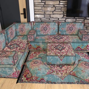 Puede incluir: Un juego de sofá seccional y alfombra a juego con un estampado floral turquesa y burdeos. El sofá tiene múltiples secciones e incluye una mesa de centro y dos otomanas cuadradas. La alfombra es rectangular y tiene un borde negro.