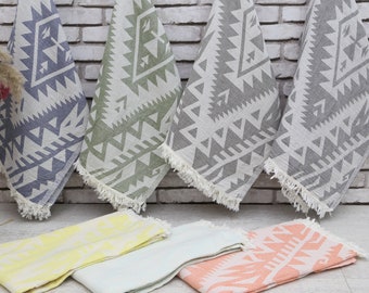 May include: Five different patterned Turkish towels, or peshtemal, in various colors, including gray, green, yellow, light blue, and orange. The towels are folded and arranged on a white surface.