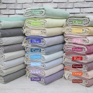 May include: A stack of folded Turkish towels in various colours, including green, navy, black, brown, grey, light grey, dark grey, dark green, apple, pistachio, beige, blue, teal, turquoise, baby blue, violet, purple, olive, mustard, pink, fuchsia, red, burgundy, orange, and burnt orange.