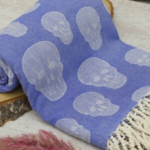May include: A blue cotton Turkish towel with a white skull pattern and white fringe.