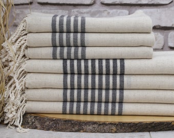 May include: A stack of white towels with black stripes and fringe. The towels are folded and stacked on a wooden surface.