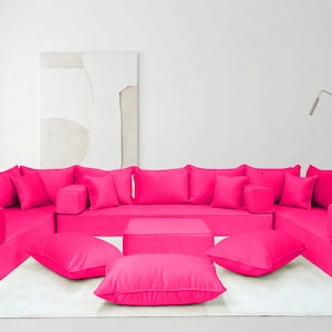 Puede incluir: Una taza de cerámica blanca con asa negra y el texto "But First, Coffee" en negrita negra. La taza se encuentra sobre un fondo borroso, sugiriendo un ambiente acogedor.