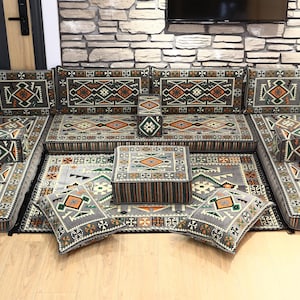 May include: A modular sofa set with a geometric pattern in shades of gray, orange, and green. The set includes multiple seat cushions, backrests, and throw pillows. The sofa is arranged in a U-shape, with a matching ottoman and rug.